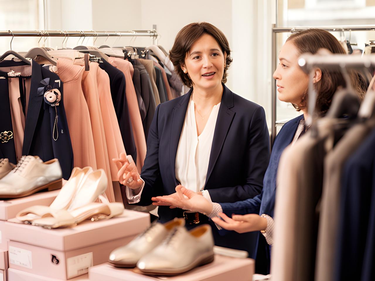A consultant speaking with a client beside rails of formal accessories and boxed shoes in a London studio